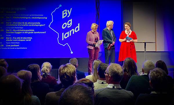 de tre lederne står foran publikum og hilser velkommen