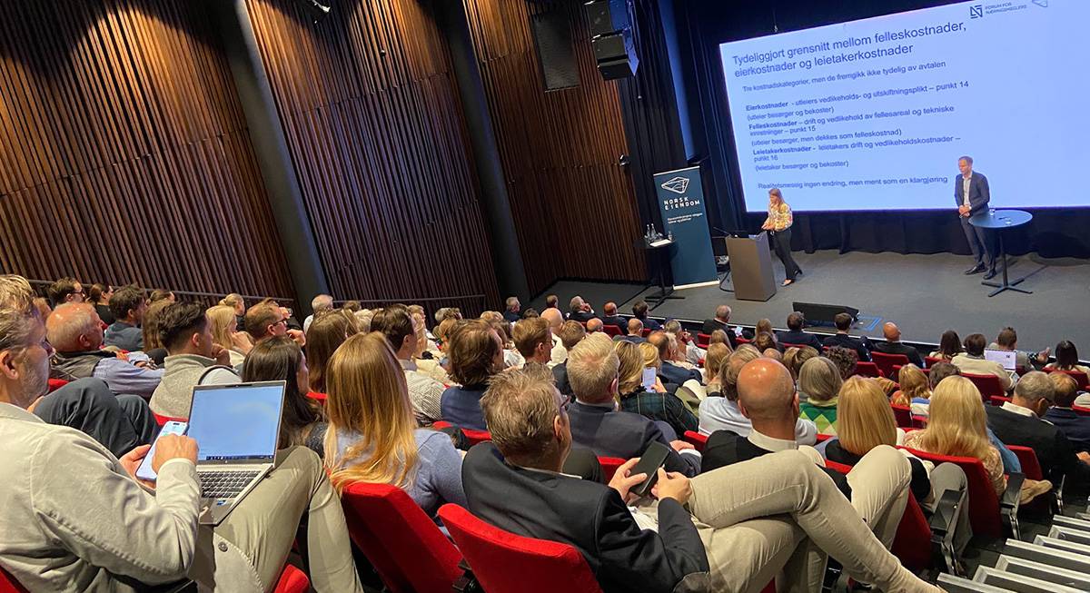 fullsatt auditorie med publikum fotografert bakfra med scenen langt der nede og to foredragsholdere med presentasjon